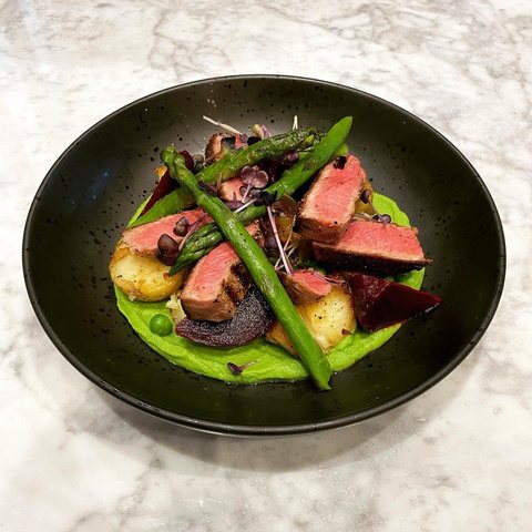 Sliced beef plated with asparagus and vegetables on a dark plate.