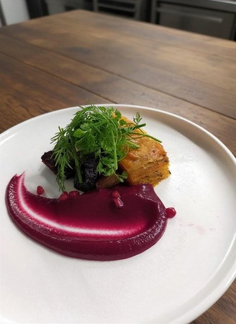 A composed plate with a sweep of beetroot purée and dressed herbs.