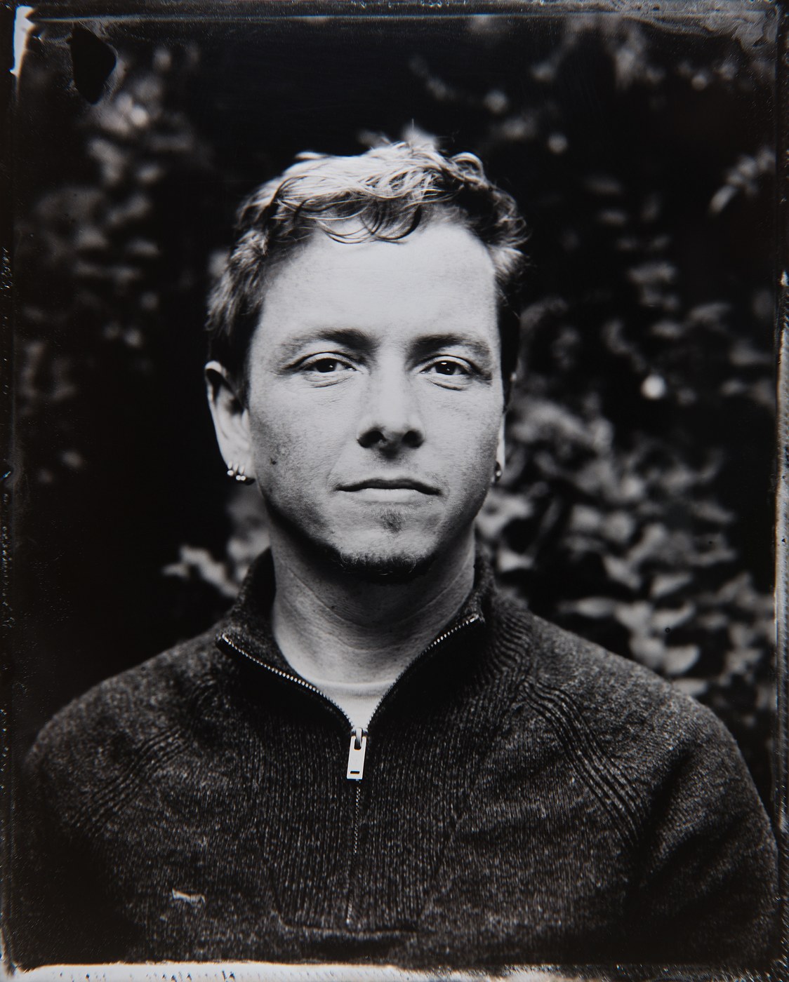 Ciarán Keogh in a wet-plate collodion portrait: black and white, looking directly at the camera, foliage behind him.